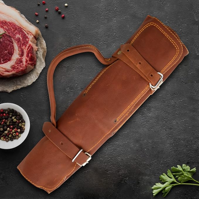 Closed cognac leather knife roll case with a carry strap beside steak and peppercorns