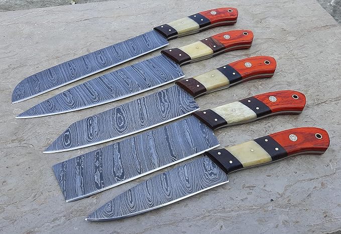 Damascus steel chef knives with orange pakka wood and cream bone handles fanned on a stone surface