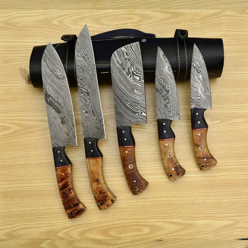 Five Damascus knives standing in front of a black leather roll with a handle