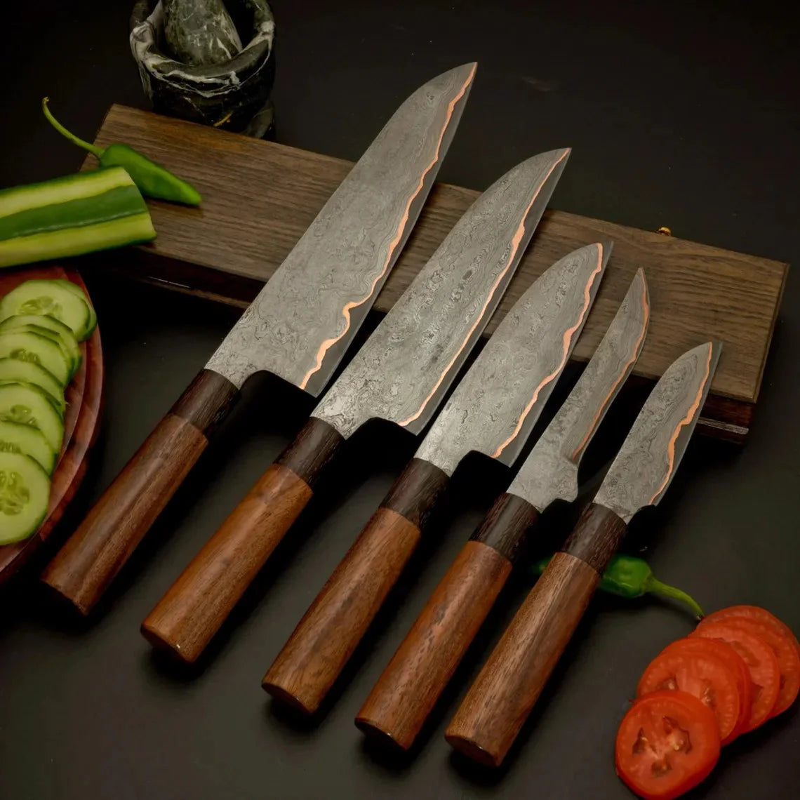 5 pieces Damascus steel kitchen knife set featuring wood handles arranged on a wooden board with sliced vegetables and tomatoes