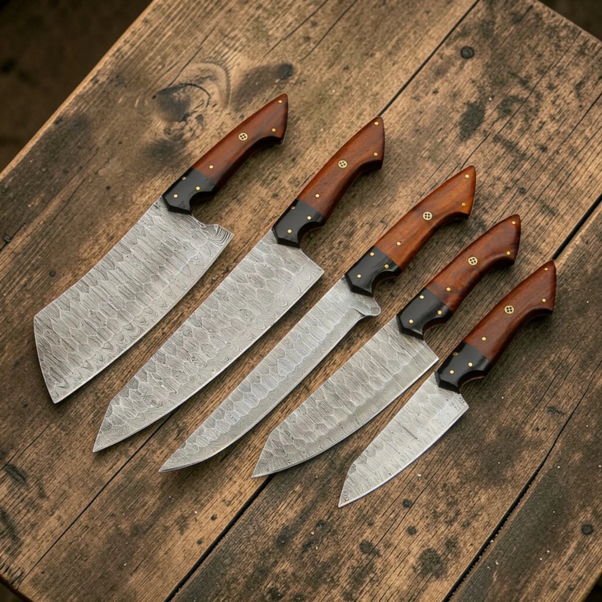 Hand forged Damascus steel chef knife collection arranged in a neat row on a wooden surface