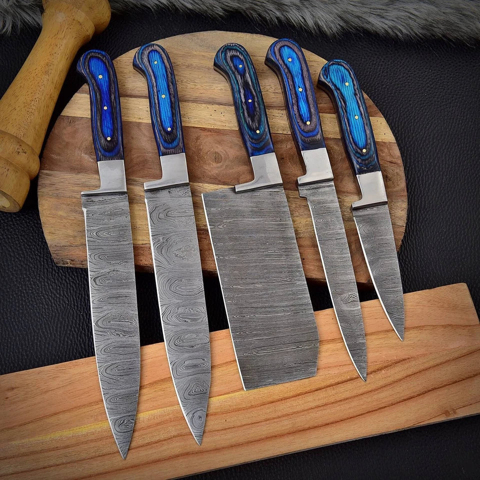 5 piece Damascus steel knife set with blue pakka wood handles arranged on wooden boards