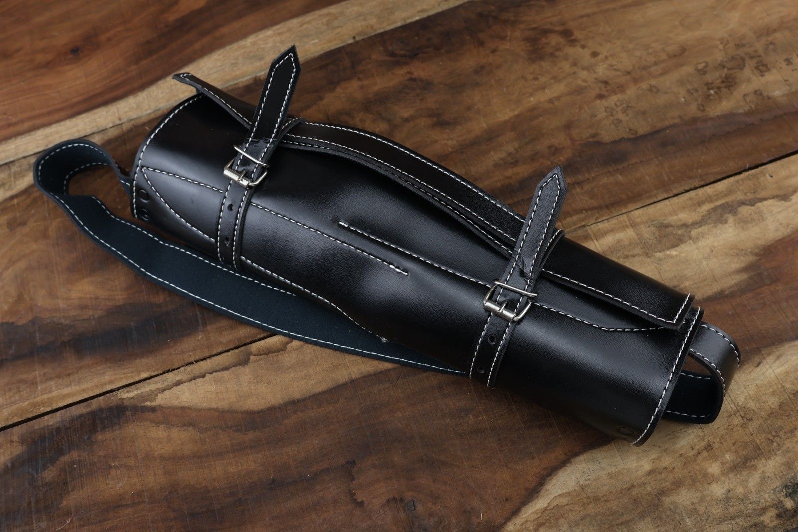 Professional Damascus steel knife collection including custom leather sheaths, displayed on a rustic outdoor surface, highlighting rugged bushcraft design.