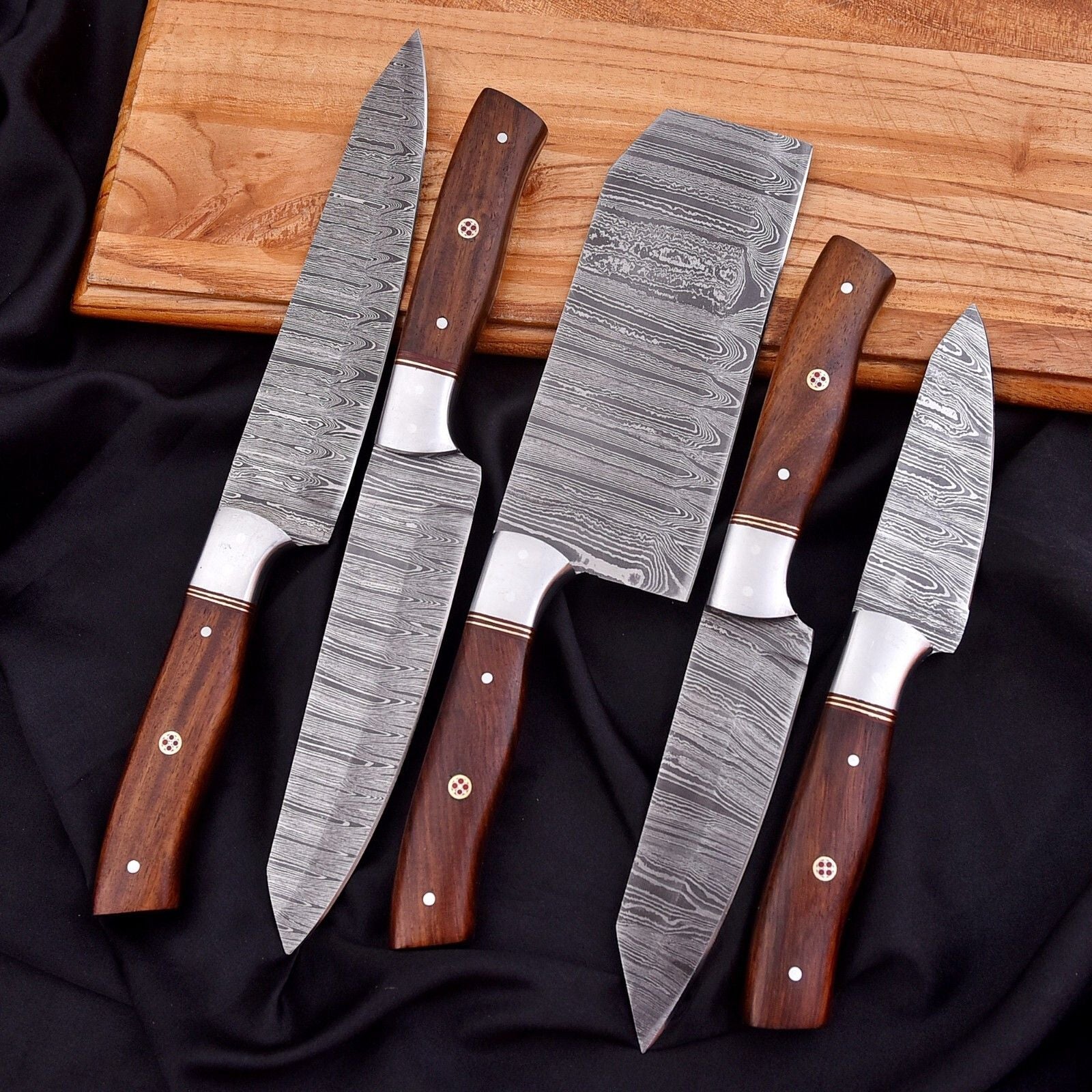 Hand forged 5 pieces Damascus steel culinary knife set arranged on a natural wood surface, highlighting professional balance and edge quality