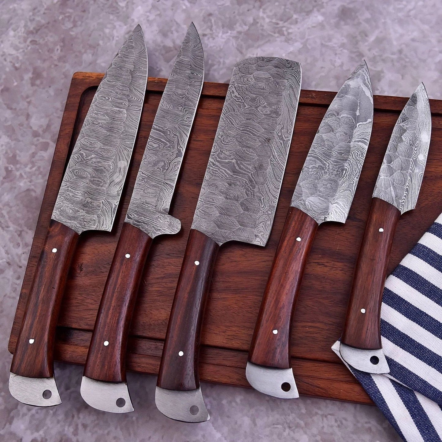 5 pc custom Damascus steel kitchen knife set featuring hand forged blades and decorative mosaic pin handles arranged on a wooden board.