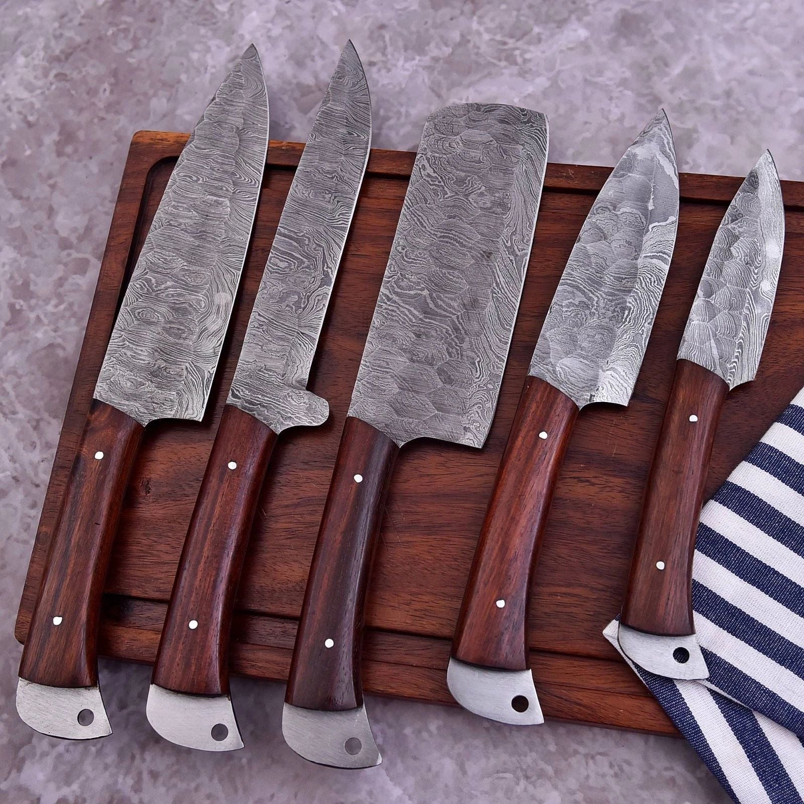 5 pc custom Damascus steel kitchen knife set featuring hand forged blades and decorative mosaic pin handles arranged on a wooden board.