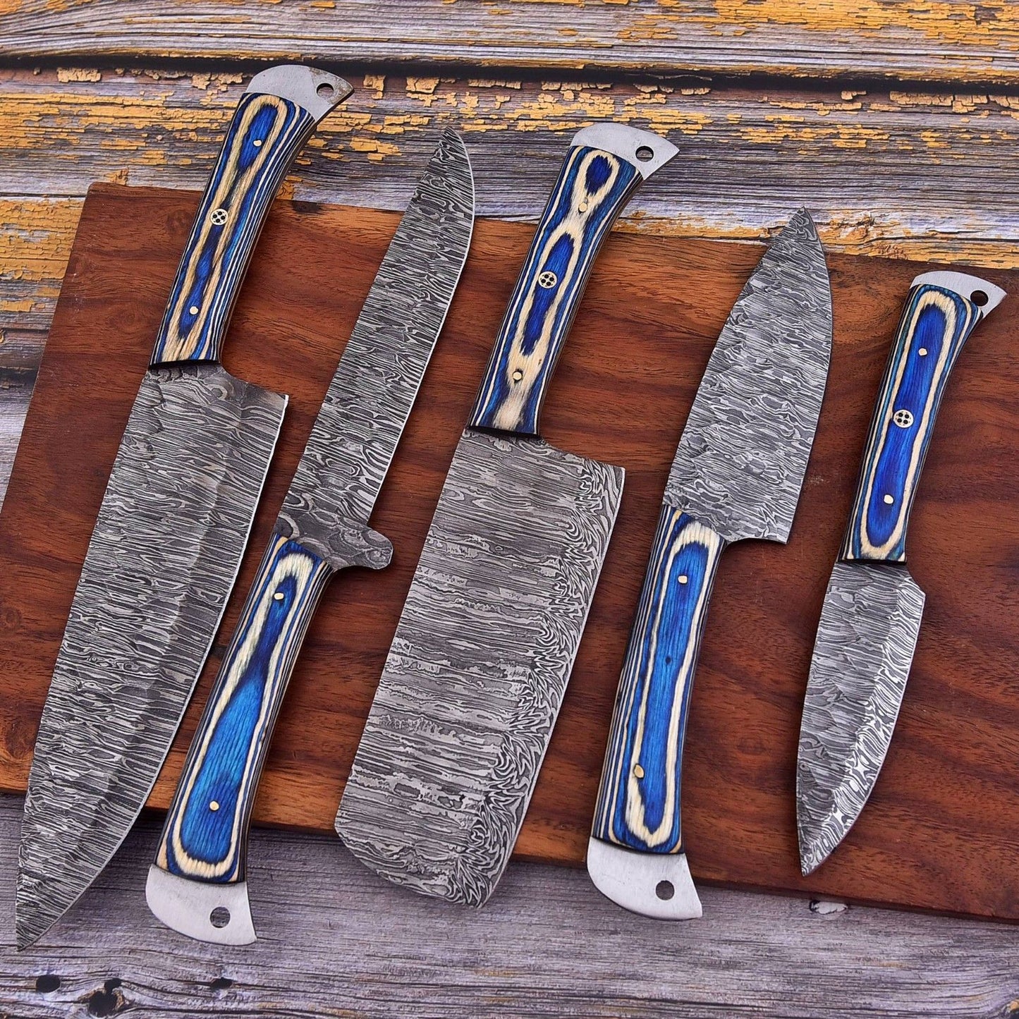 Artisanal Damascus kitchen knife set displayed on a rustic wood surface, highlighting the contrast between the bone handles and forged steel blades.