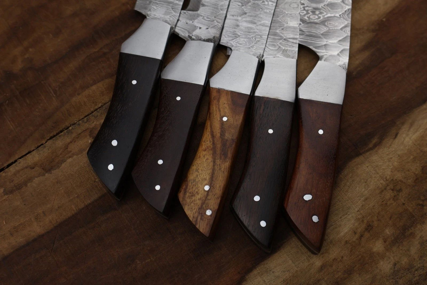 Close up view of a premium hardwood handle featuring a decorative brass mosaic pin and hand casted steel bolster on a Damascus steel knife.