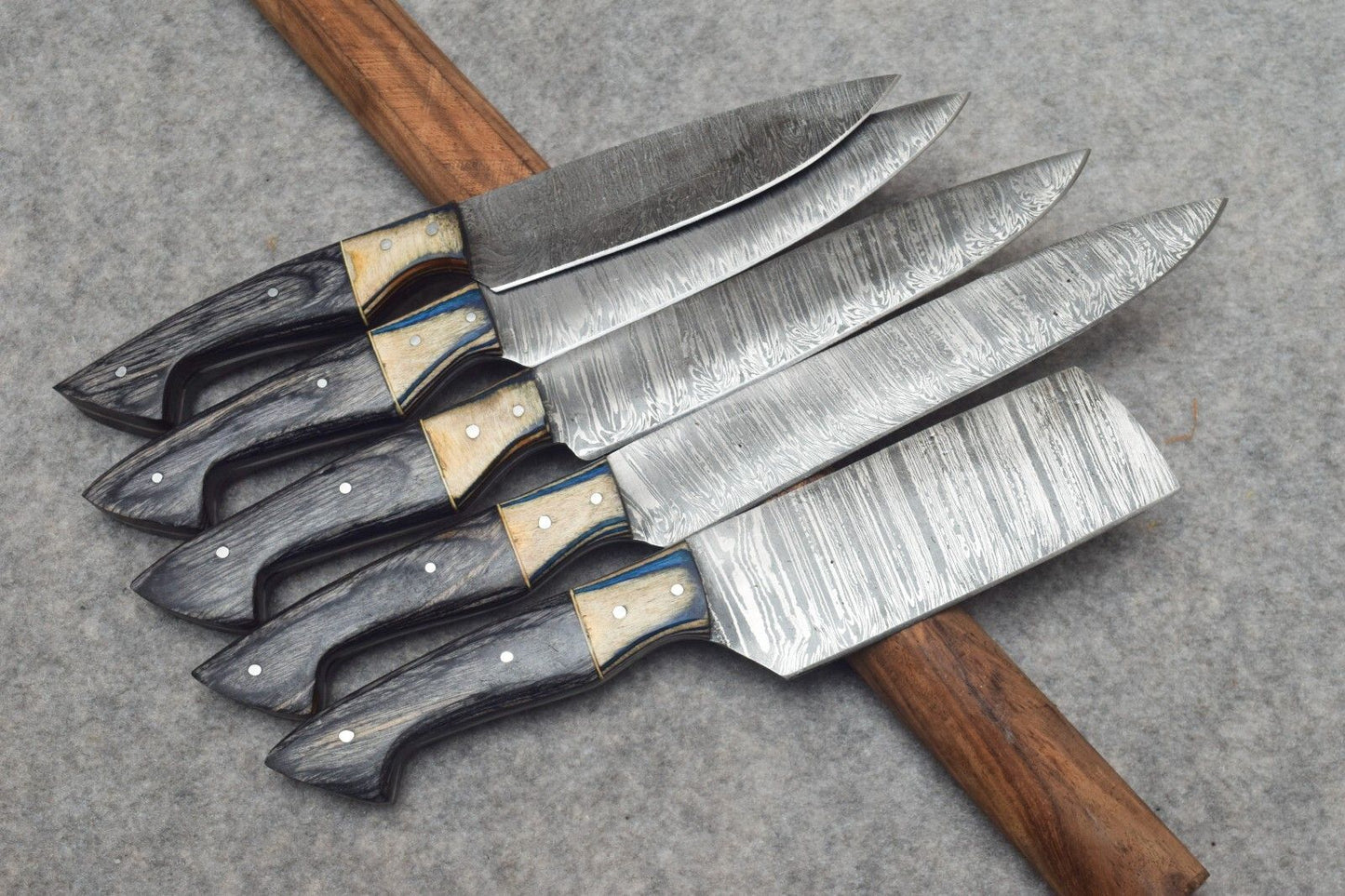 Professional Damascus steel kitchen knives displayed in a forest themed setting, highlighting rugged design and high performance forged steel.