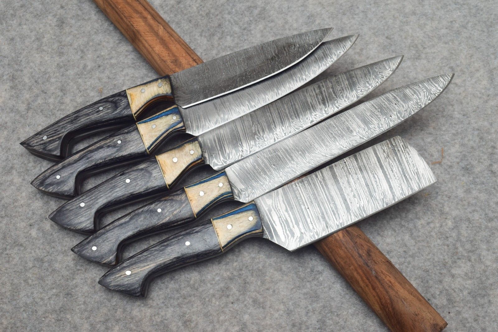 Professional Damascus steel kitchen knives displayed in a forest themed setting, highlighting rugged design and high performance forged steel.