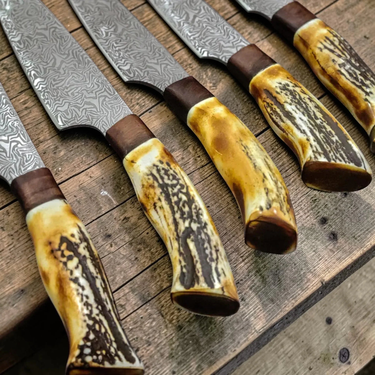 Close up view of the antler handles and bolster details on a custom Damascus steel kitchen knife collection