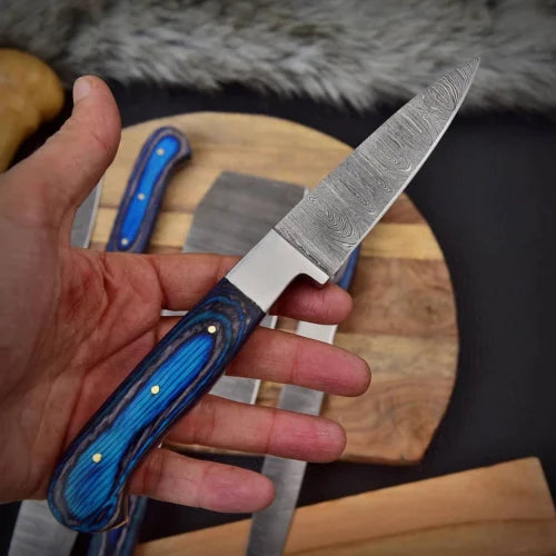 Close up view of a custom Damascus steel utility knife being held, showcasing the handle and blade pattern