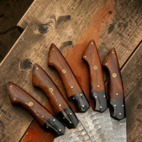 Close up view of custom Damascus steel knife handles lined up on a rustic wooden background