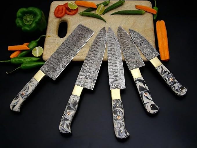 Damascus steel knife set with black and gray marbled acrylic handles on a wood cutting board with vegetables
