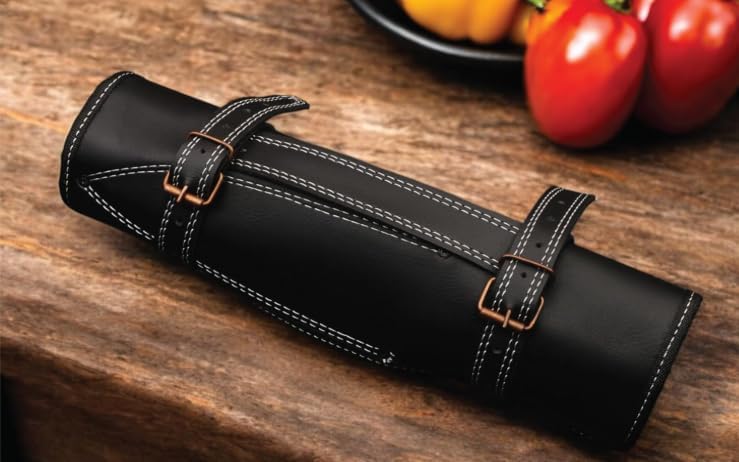 Black leather knife roll rolled shut with two copper buckles on a wooden table