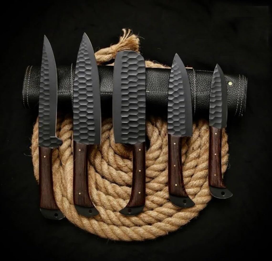 Five black kitchen knives with wood handles standing on a coiled rope