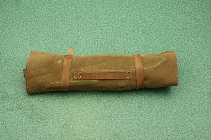 Closed tan suede knife roll case with a leather strap on a green surface