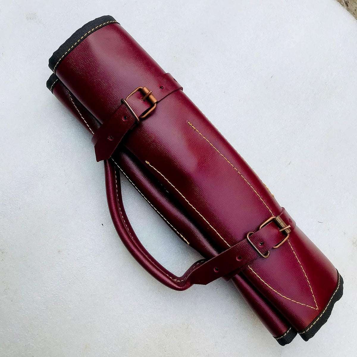 Burgundy leather knife roll buckled shut with a carry handle and copper buckles