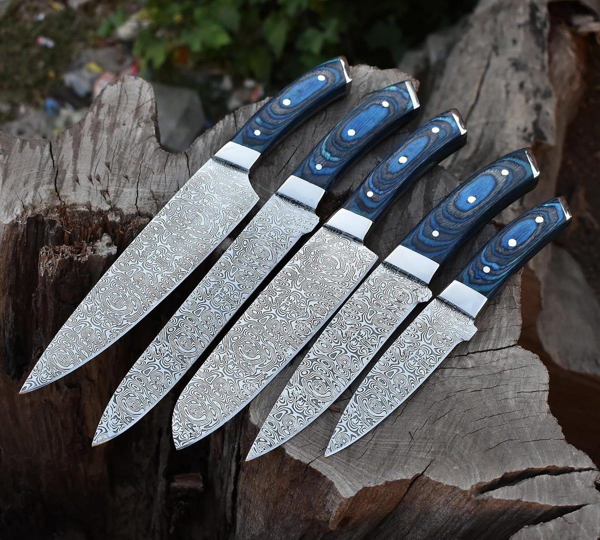 Kitchen knives with patterned blades and blue handles lined up on a stump