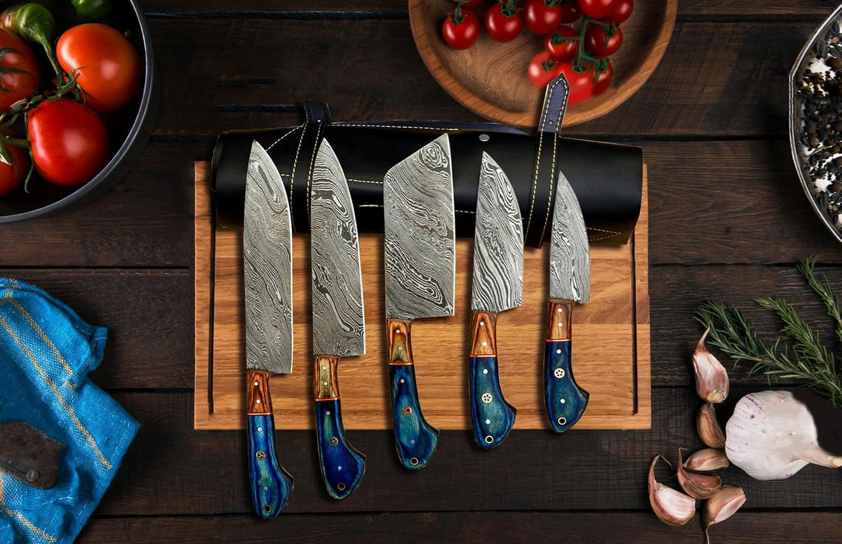Five Damascus kitchen knives standing on a board in front of a black leather roll