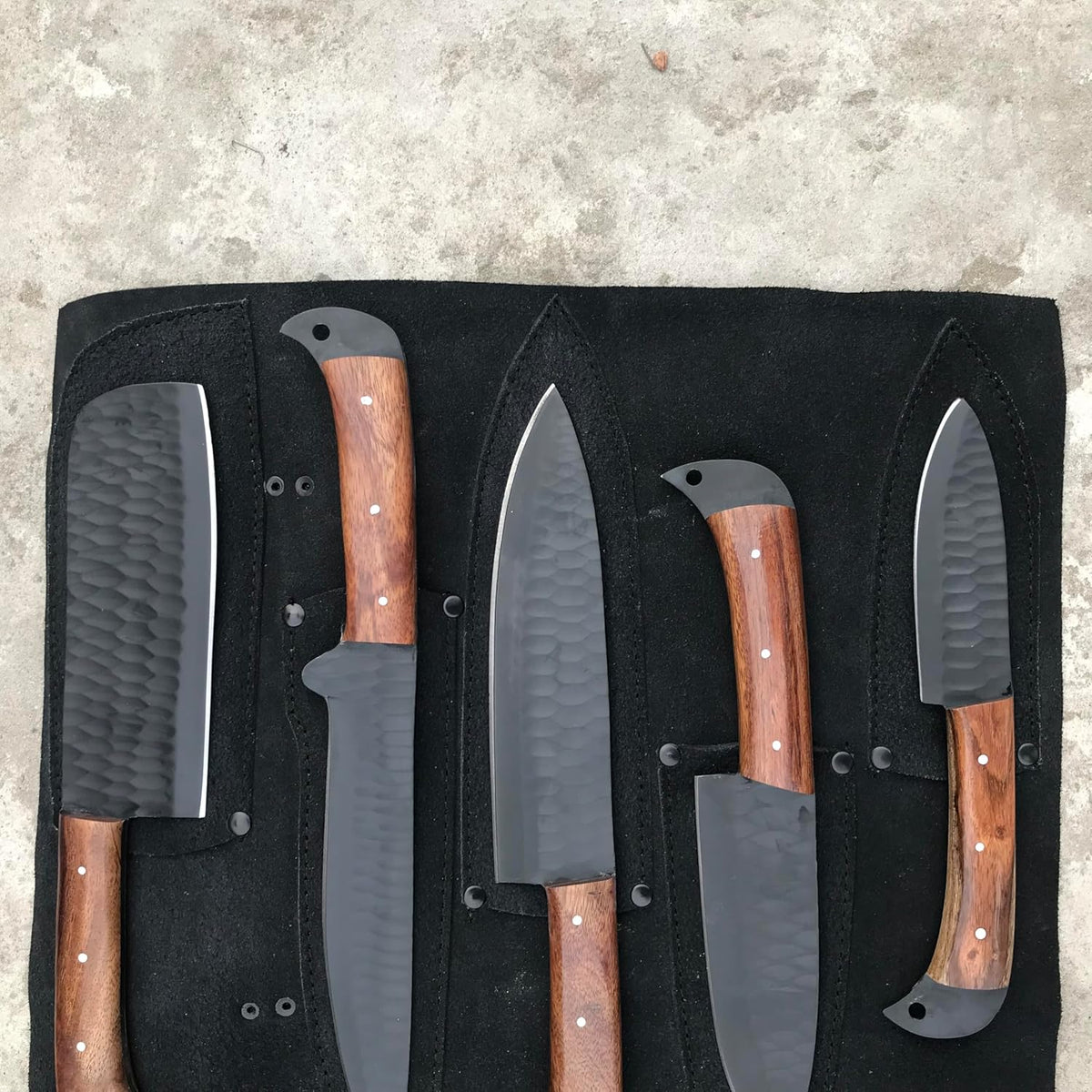 Black kitchen knives with rosewood handles resting on an open black leather knife roll