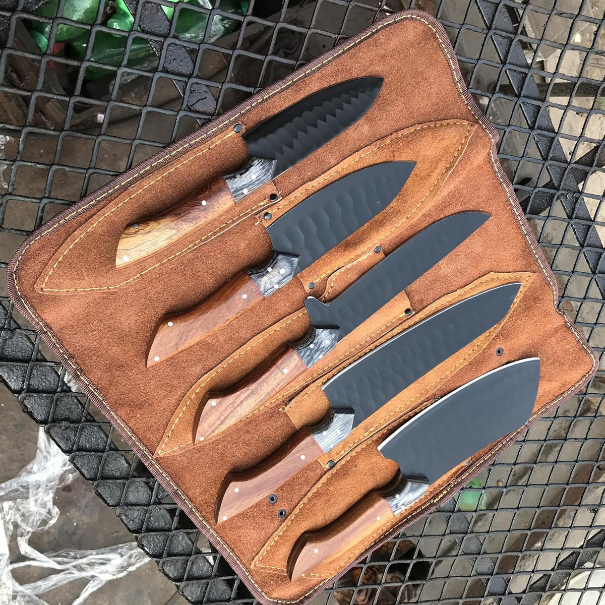 Open leather knife roll with five black kitchen knives in stitched sheaths