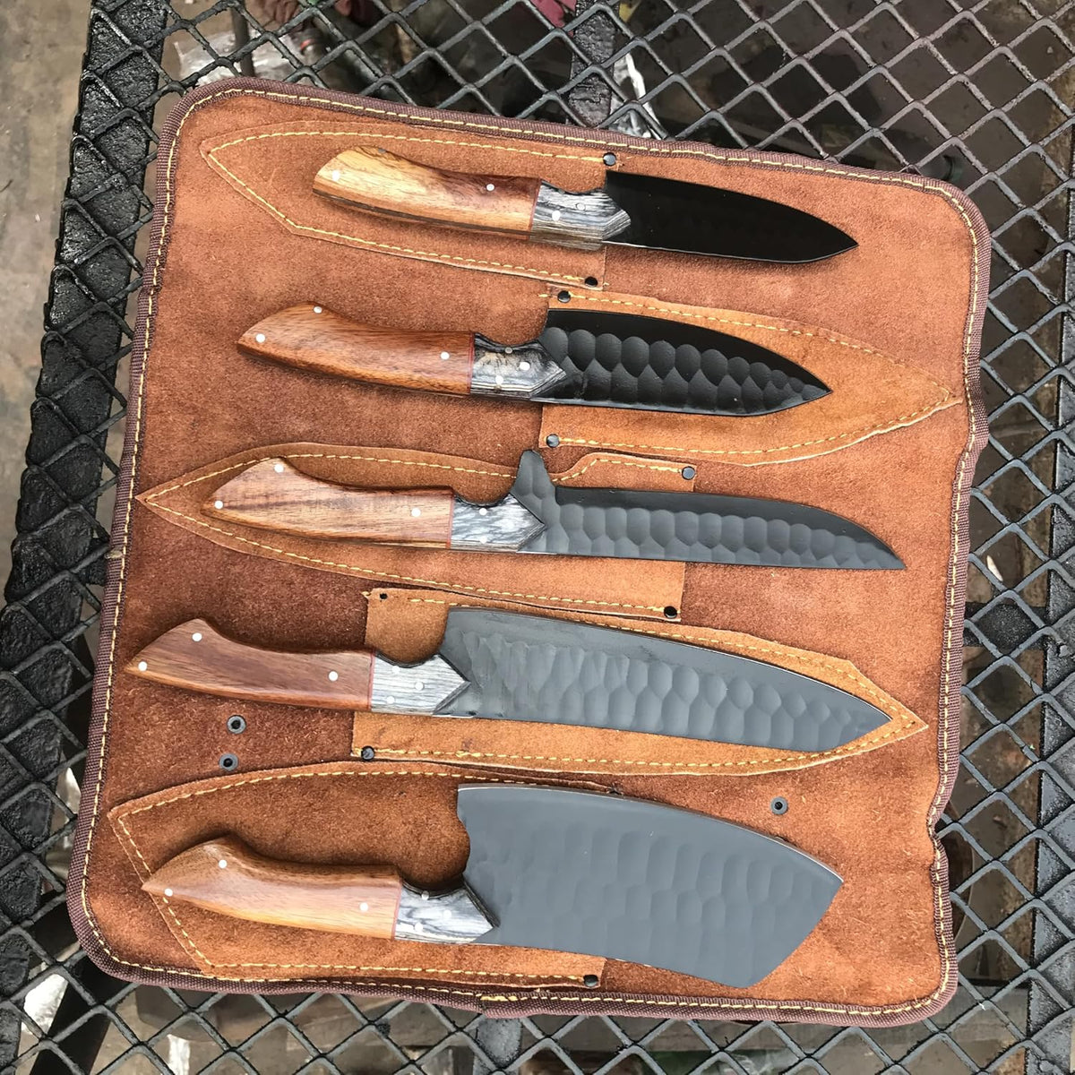 Five black kitchen knives with rosewood handles seated in a leather knife roll