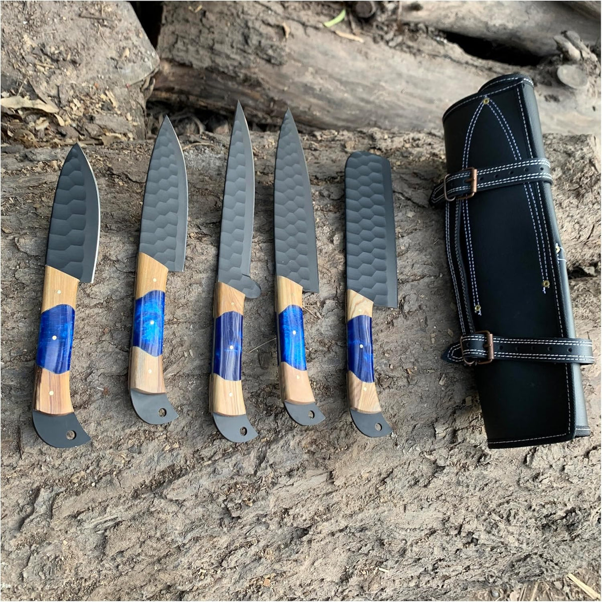 Full lineup of black finish steel blades with wood and blue resin handles on a log