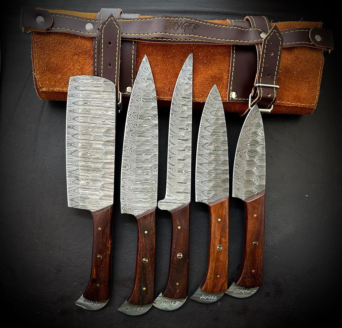 Damascus steel knife set with wood handles fanned in front of a leather roll case