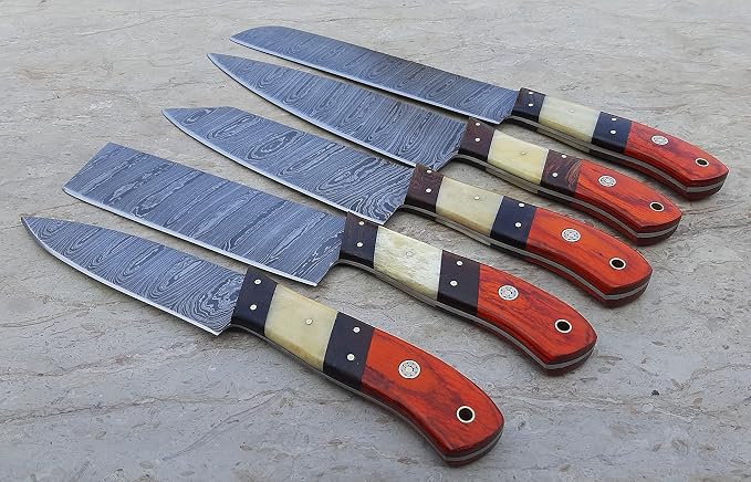 Damascus steel chef knives with orange pakka wood and cream bone handles fanned on a stone surface