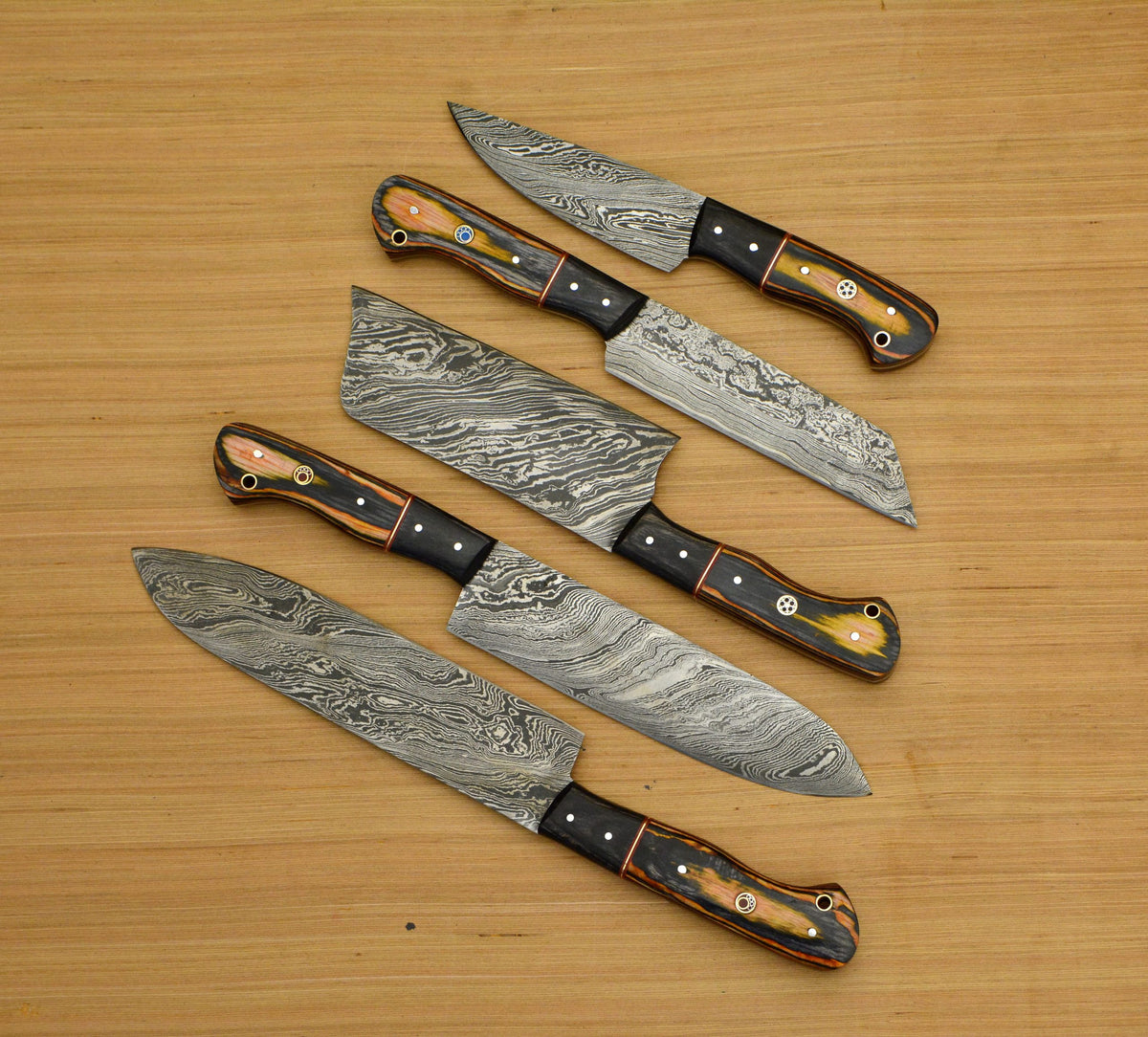 Black pakka wood handle knives with orange bolster fanned on wood table