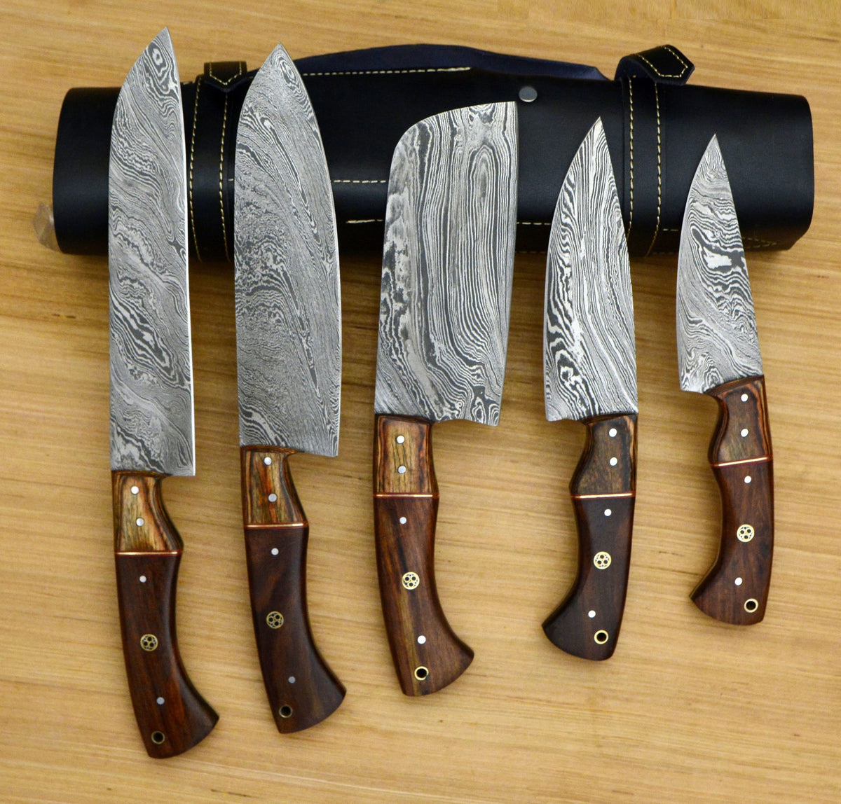 Five Damascus knives with rosewood handles standing before a black leather roll