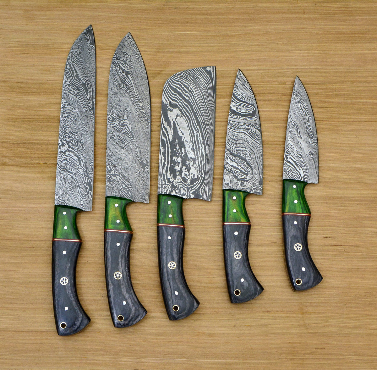 Detailed close up of Damascus steel blades and green pakkawood handles on a wooden cutting board