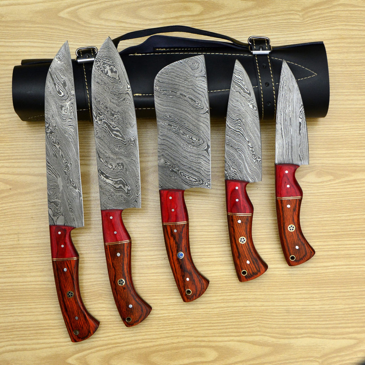 5 piece Damascus steel chef knife set laid out on wood table with leather roll case