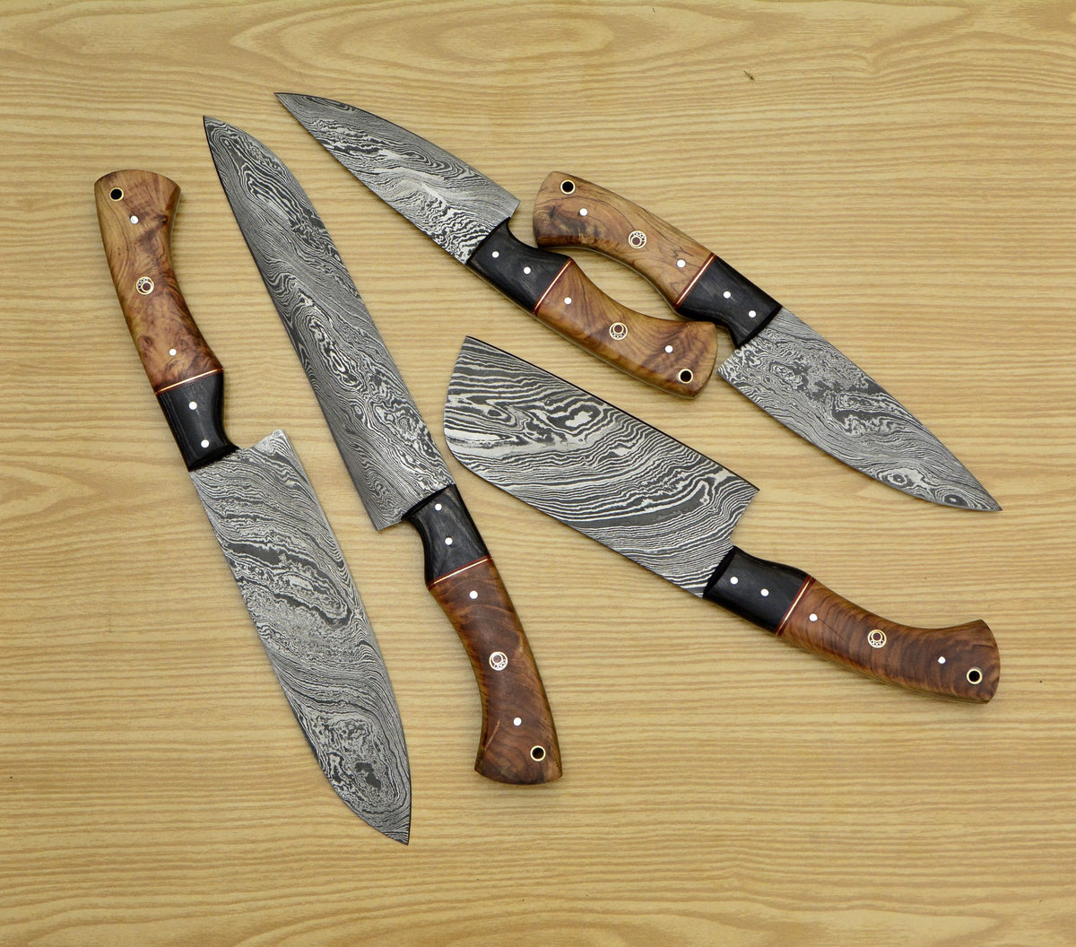 Five Damascus kitchen knives with olive wood handles on a light wood table
