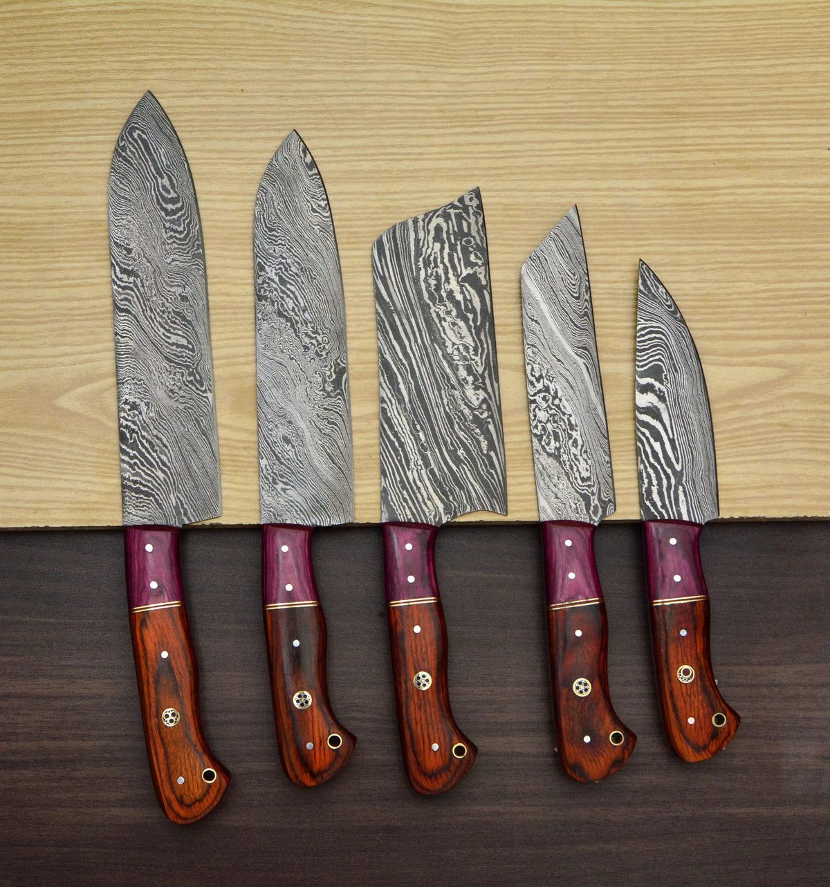 Red pakka wood knife handles with magenta bolster in a row on wood table