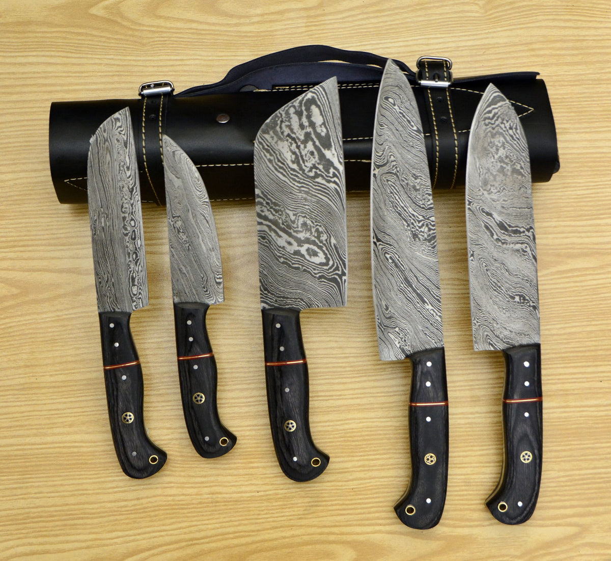 Five Damascus kitchen knives standing beside a rolled leather knife storage case