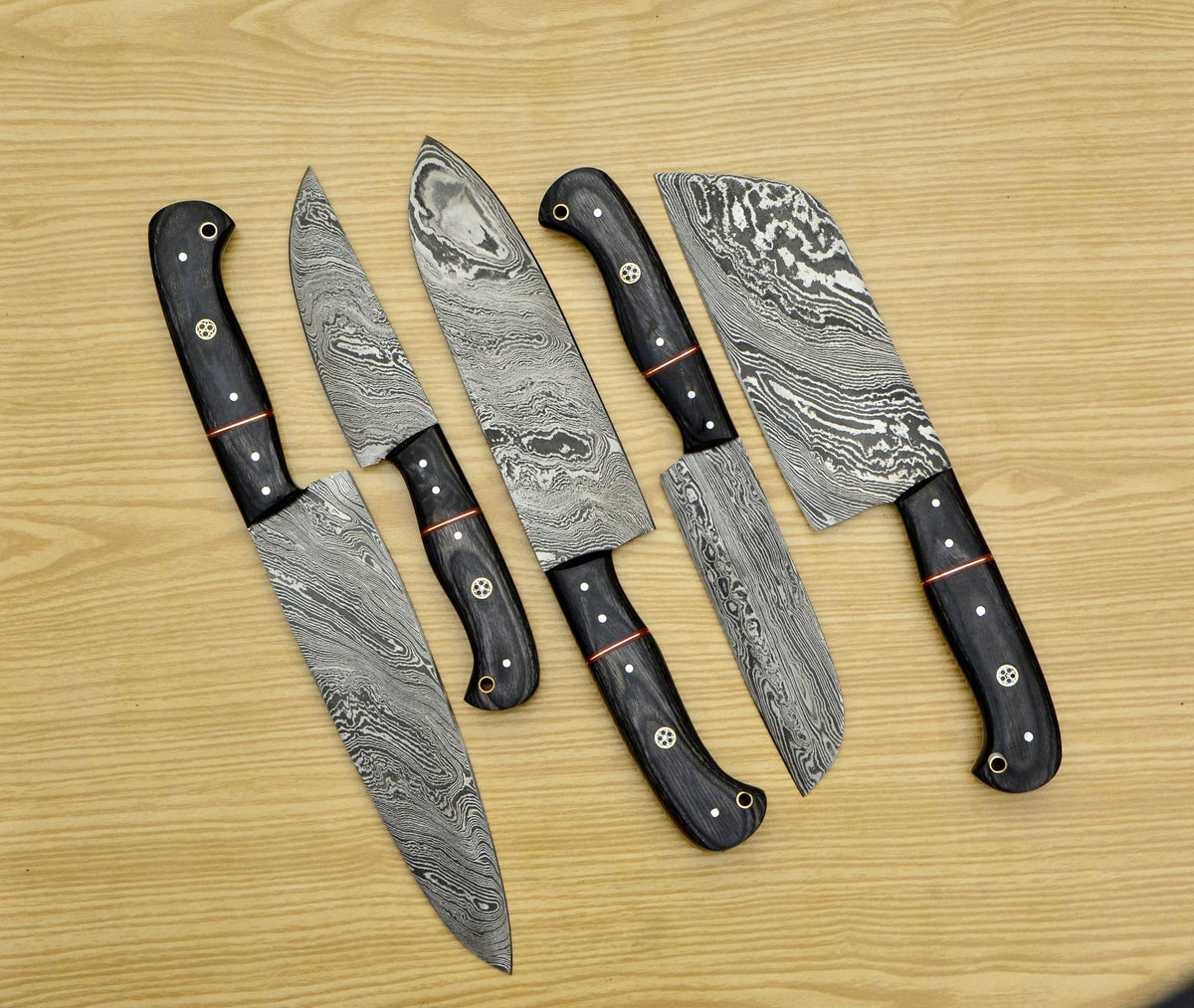 Five piece Damascus chef knife set with patterned blades and Pakkawood handles displayed on a wooden table
