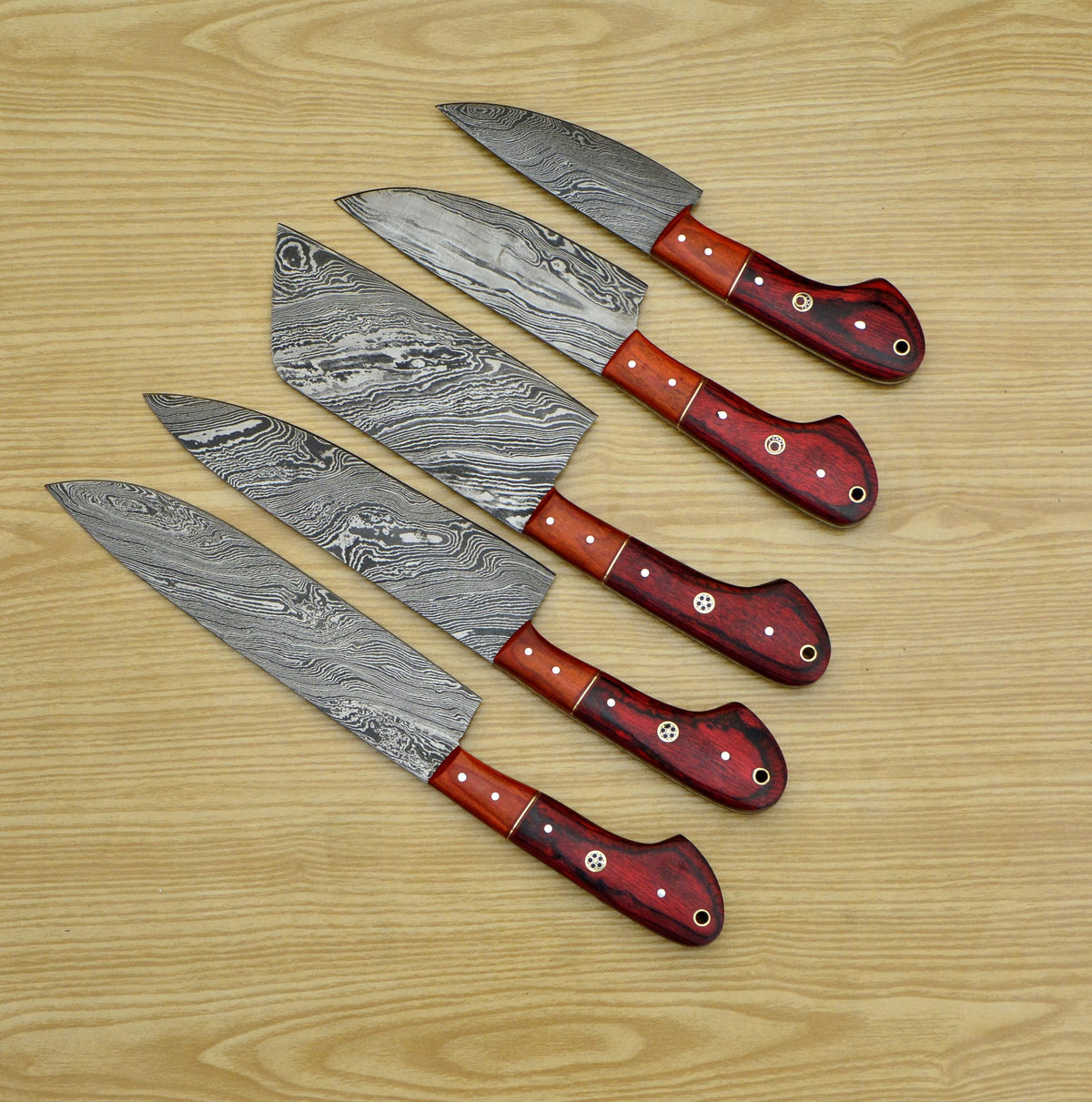 Professional culinary chef knife collection featuring patterned Damascus blades and ergonomic red handles on a wooden background