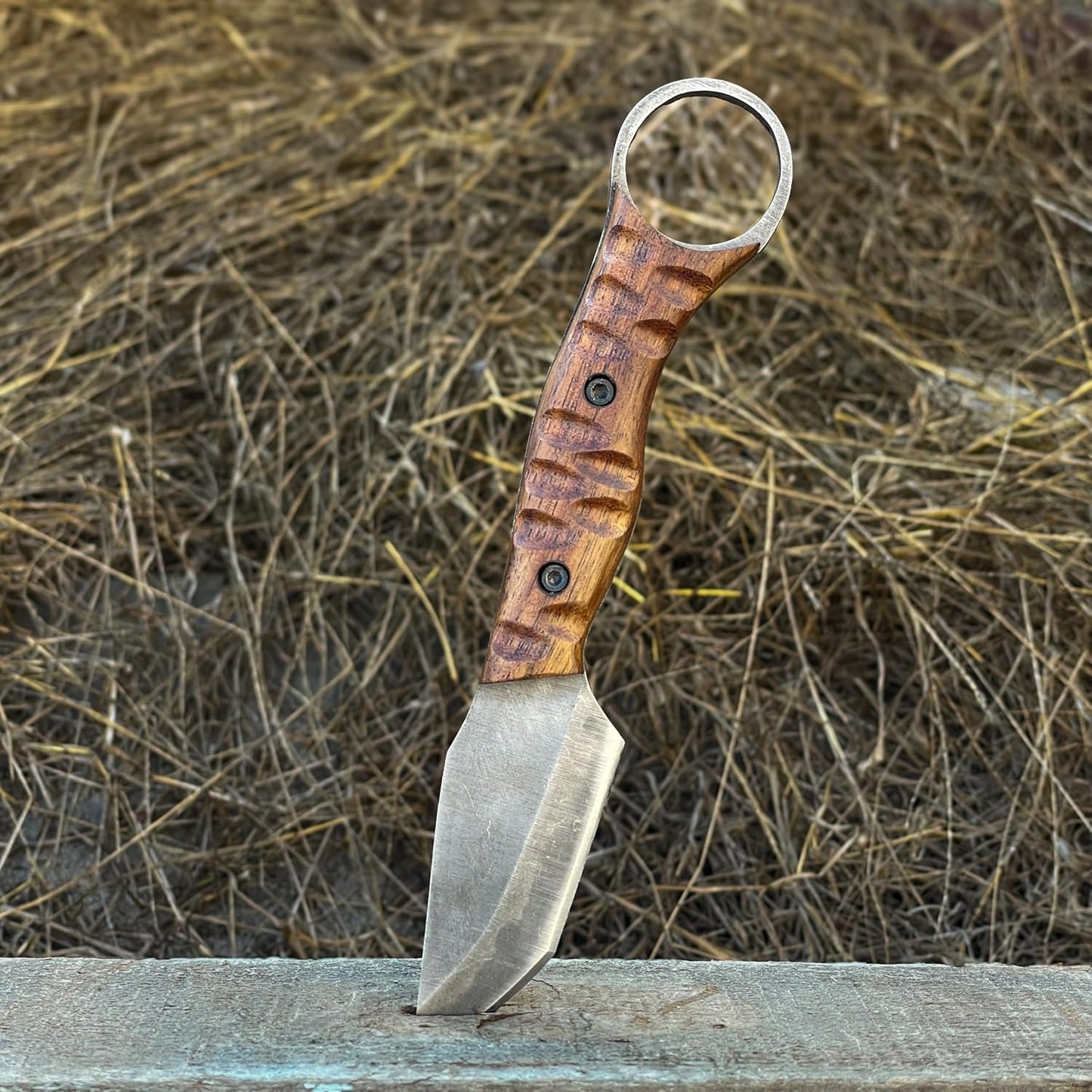 Best Bushcraft Knife standing upright in wooden beam with hay background