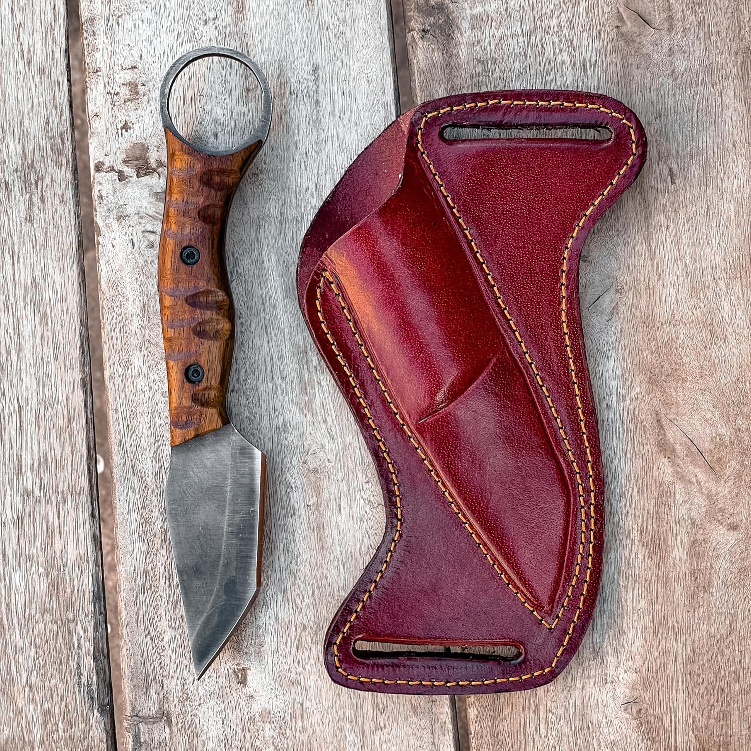 Best Bushcraft Knife with wood handle beside red leather sheath on rustic wood table