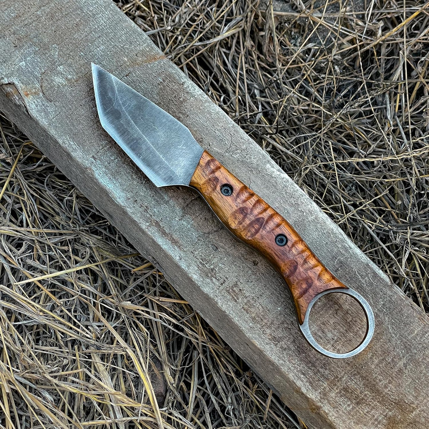 Best Bushcraft Knife with wood handle resting on wooden beam in dry grass