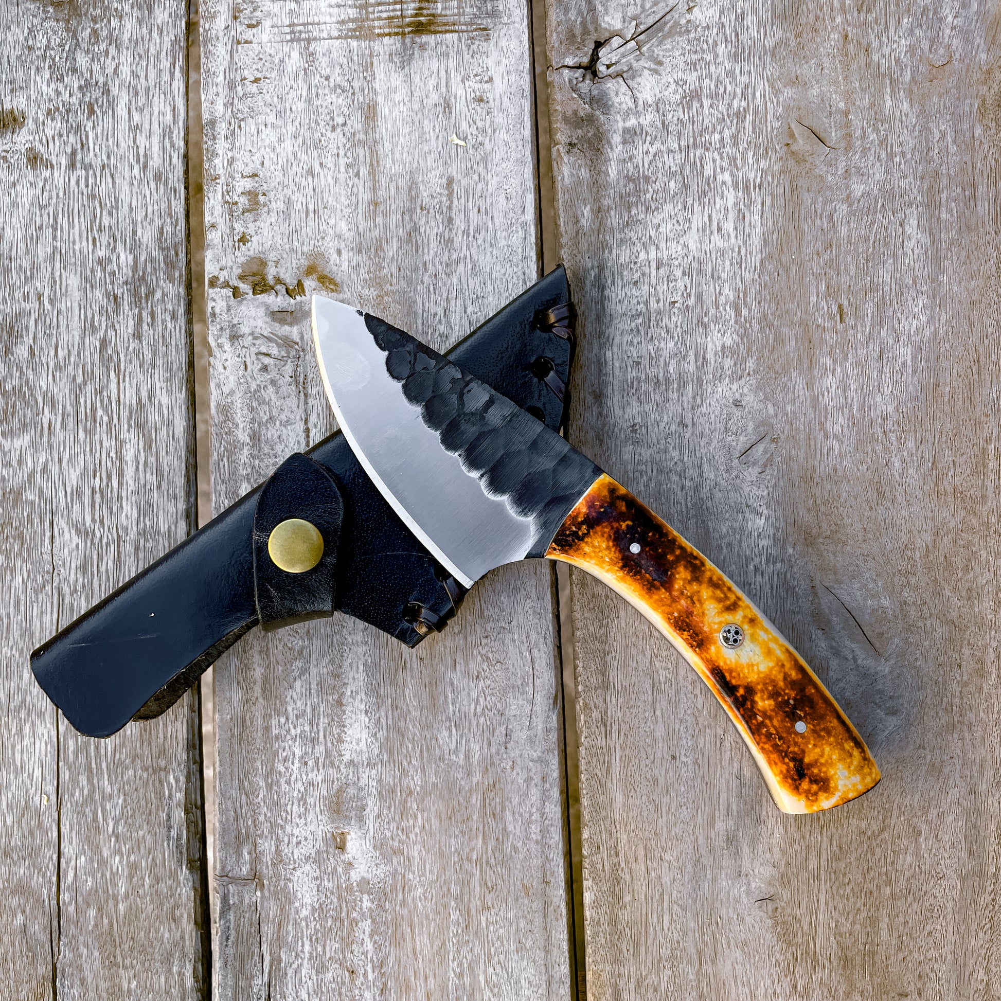 Bone Handle Skinner Knife with hammered blade on black leather sheath and wood background