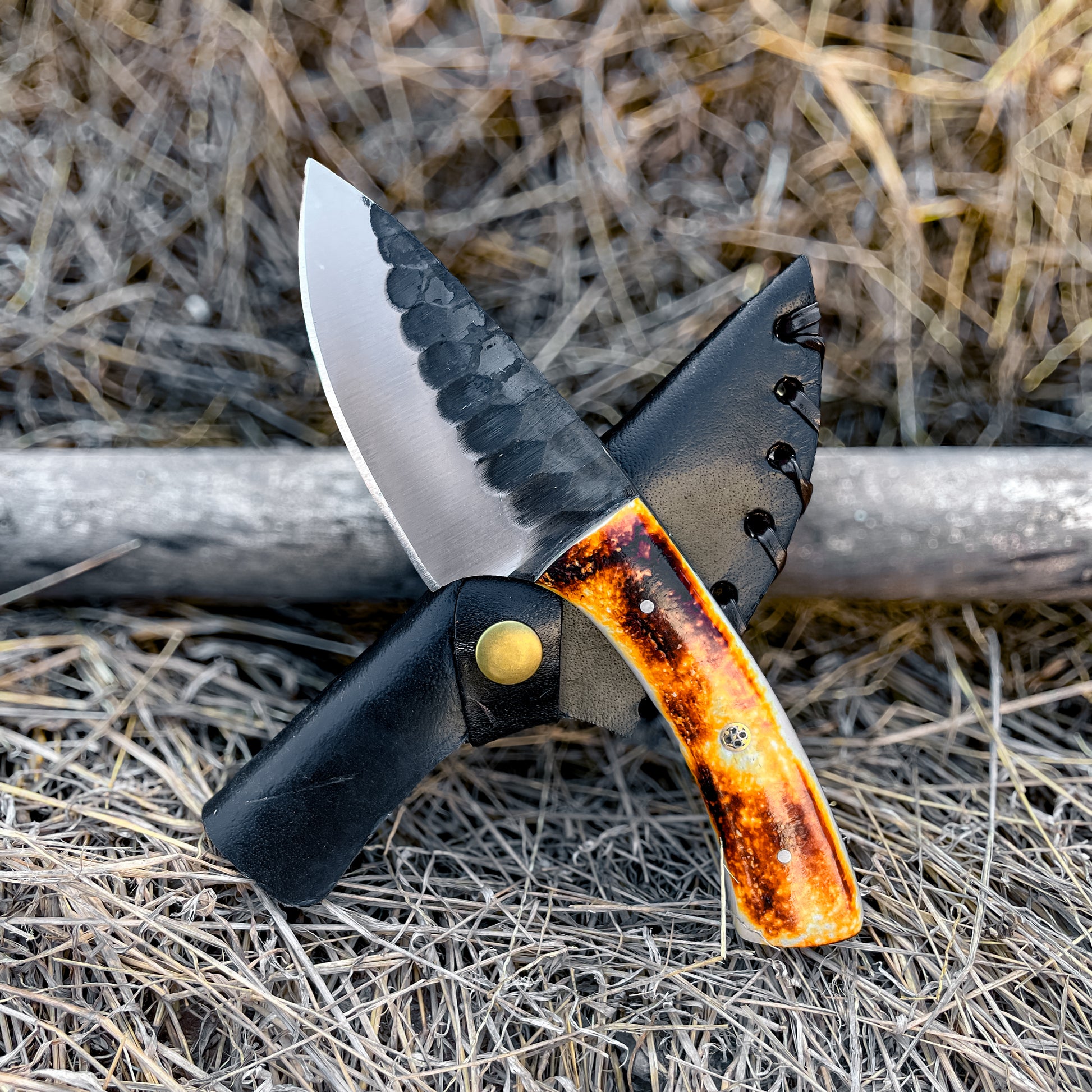 Bone Handle Skinner Knife with amber bone handle crossed over black leather sheath outdoors