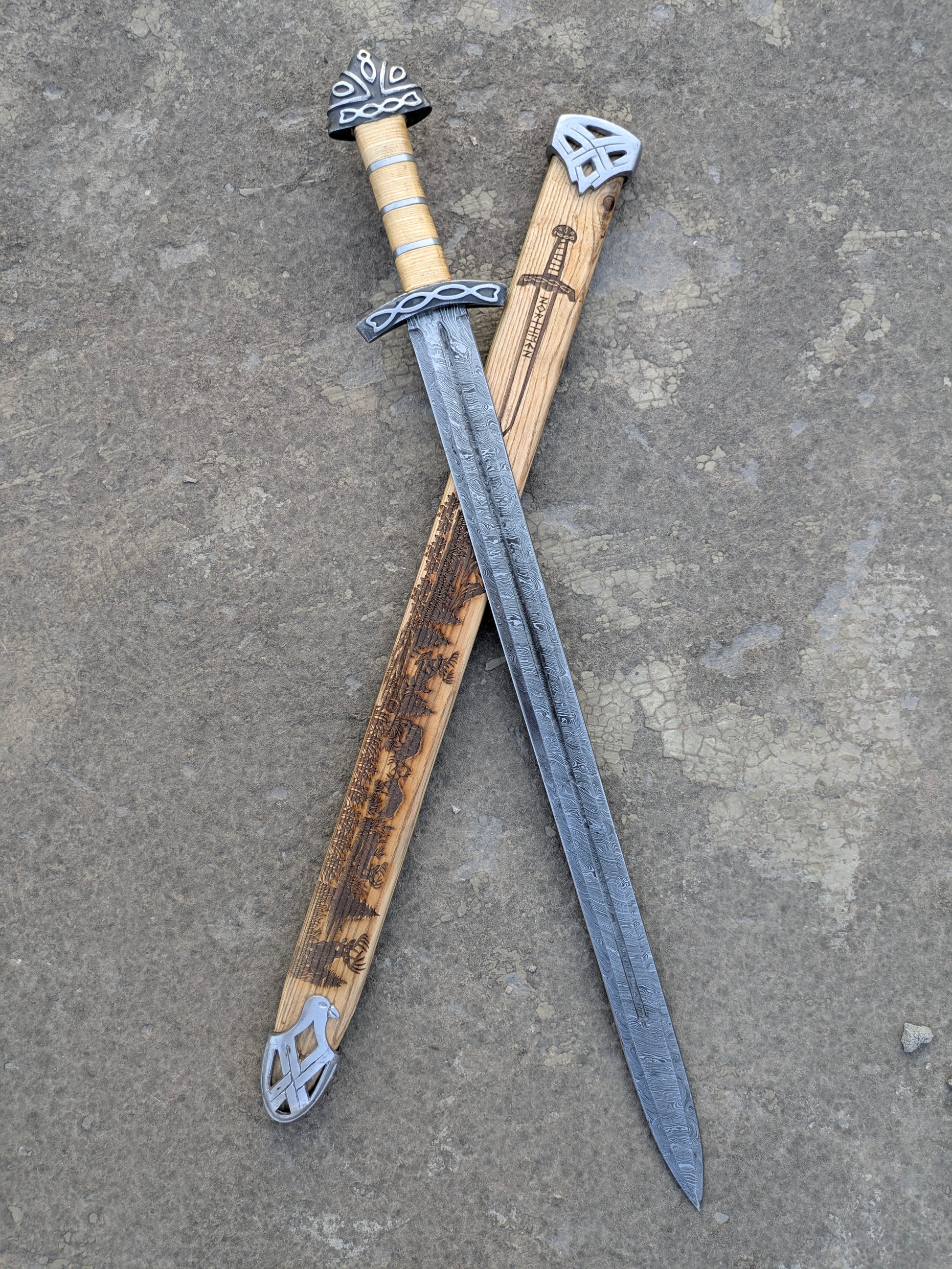 Damascus Steel Northman Viking Sword crossed with engraved wooden scabbard on stone