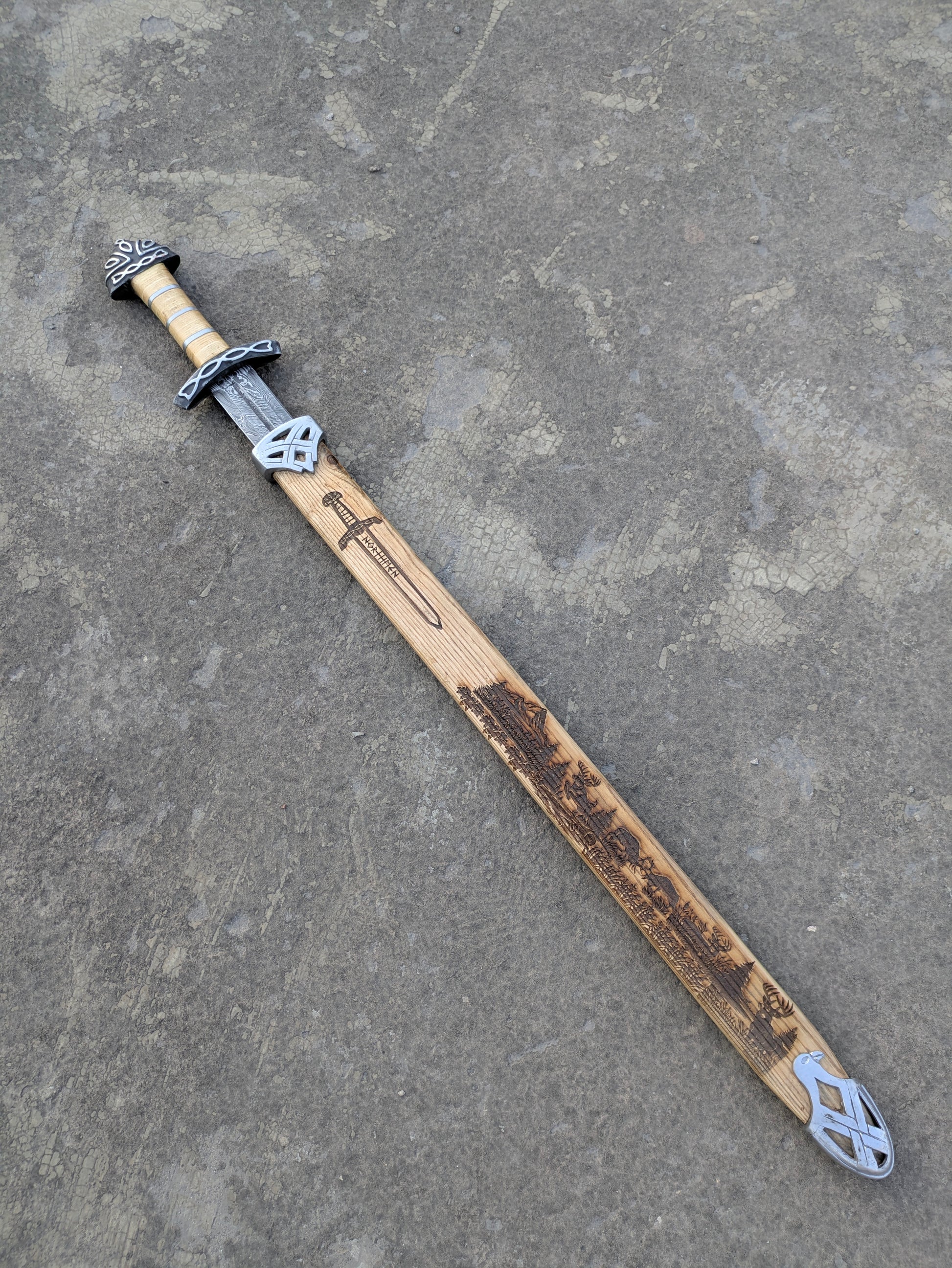 Damascus Steel Northman Viking Sword partially sheathed in engraved wooden scabbard