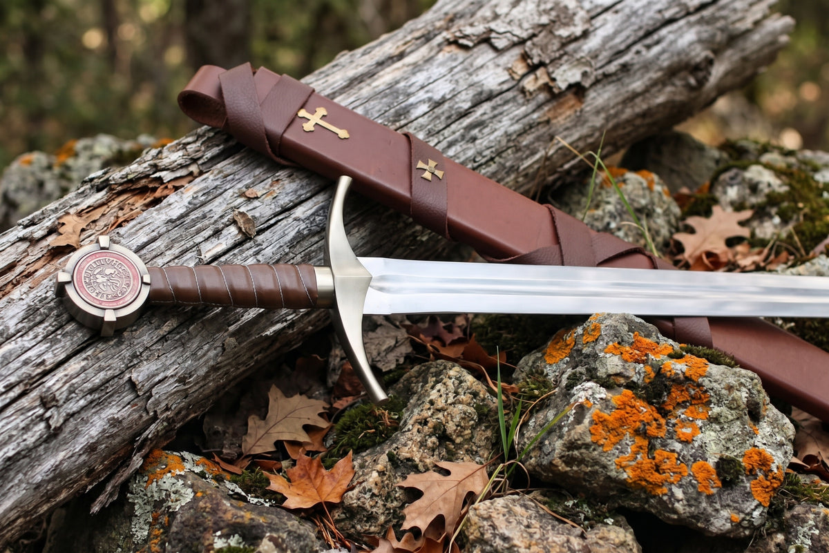 Decorative sword with red seal pommel and brown grip resting beside a brown leather sheath with a gold tone cross