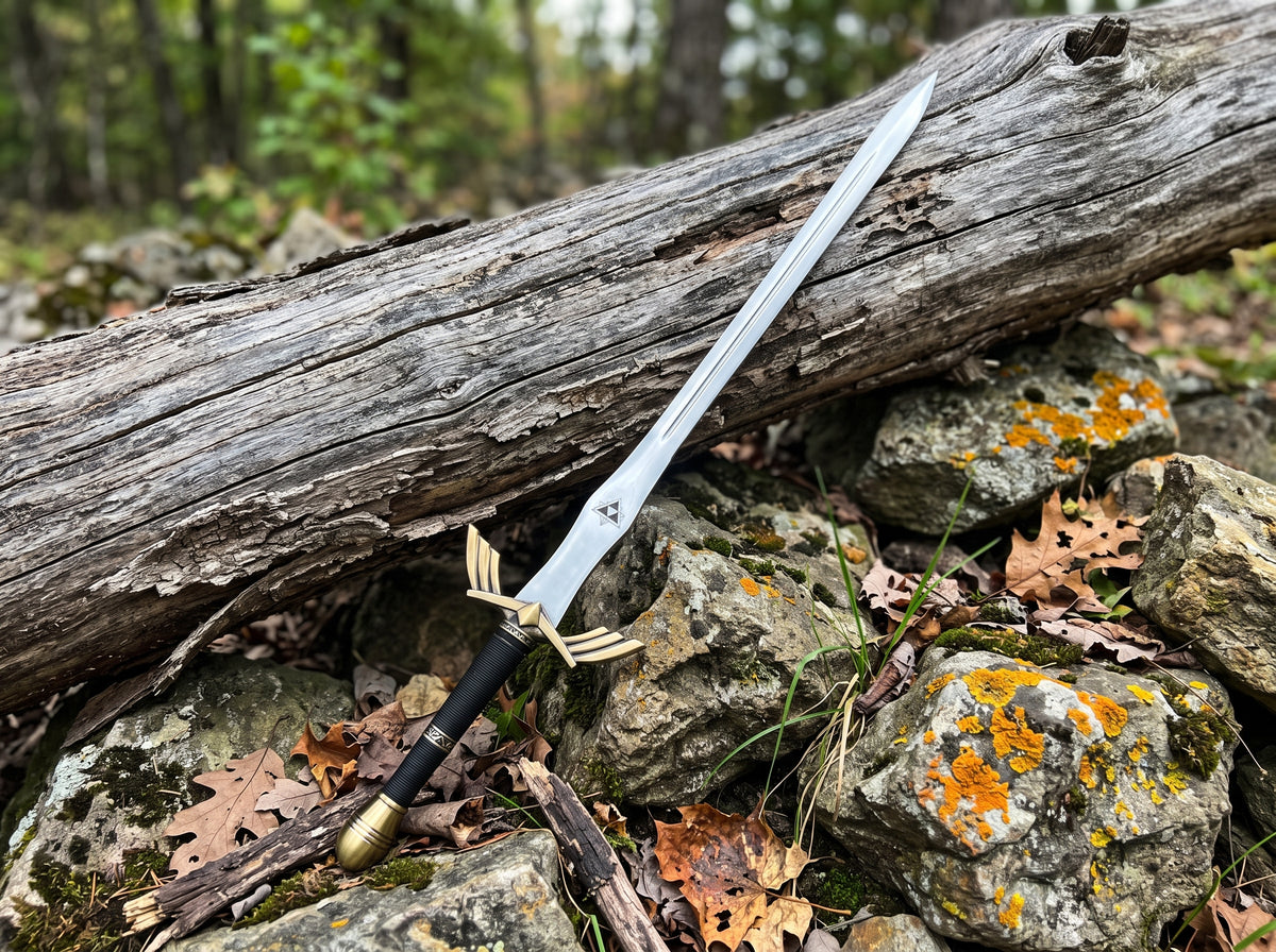 Decorative sword with winged gold tone crossguard, black cord wrapped grip and polished blade leaning on mossy rocks