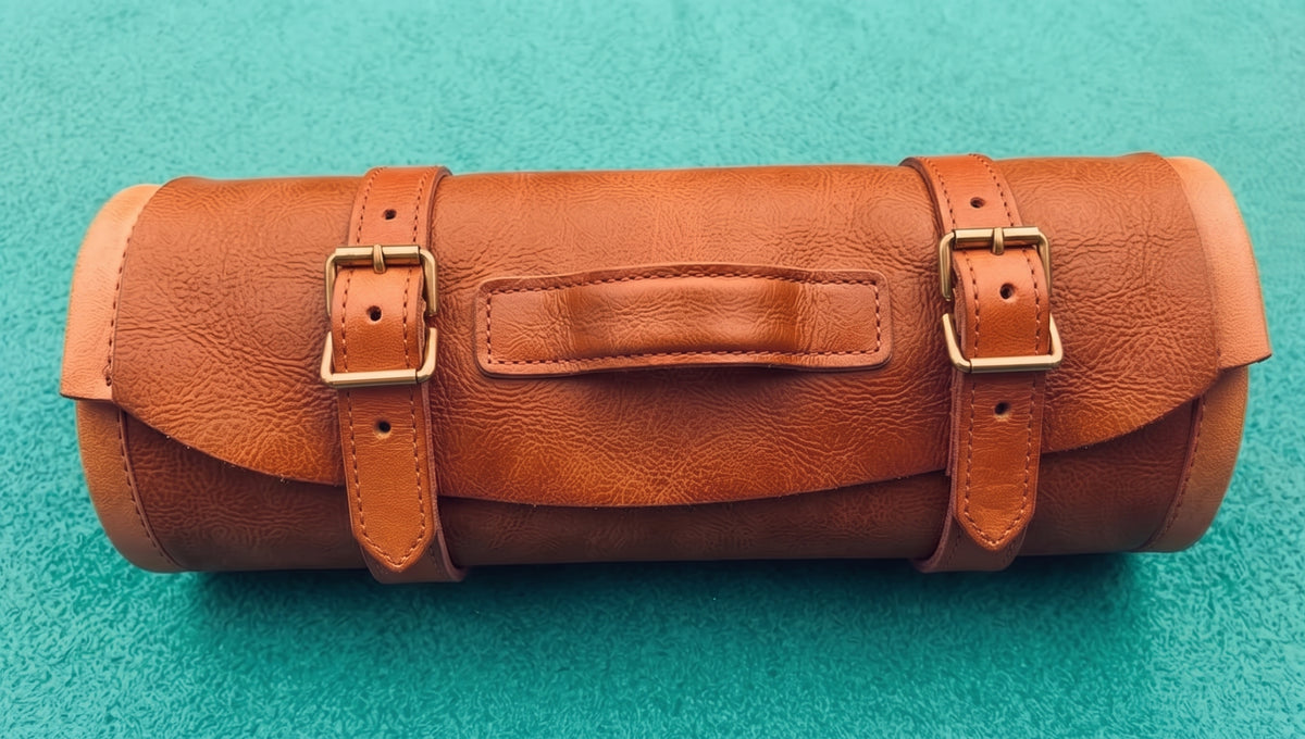Leather roll case closed and rolled up with two straps resting on teal fabric