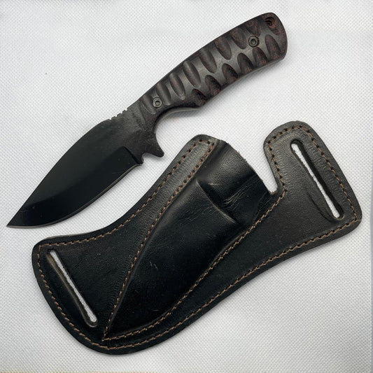 Regarded as the best skinning knife, this 8-inch fixed blade features a 4-inch powder-coated carbon steel blade with a sharp drop-point edge. The 4-inch dark Micarta handle has deep scalloped grooves for a secure grip. Resting on a white surface, it lies beside a rugged black leather pancake sheath featuring thick perimeter stitching and dual belt loop slots designed for horizontal daily carrying.